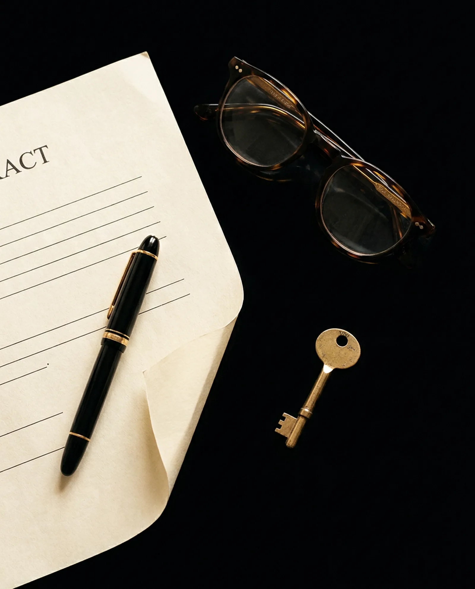 A contract, a fountain pen, reading glasses and a small gold key on black marble